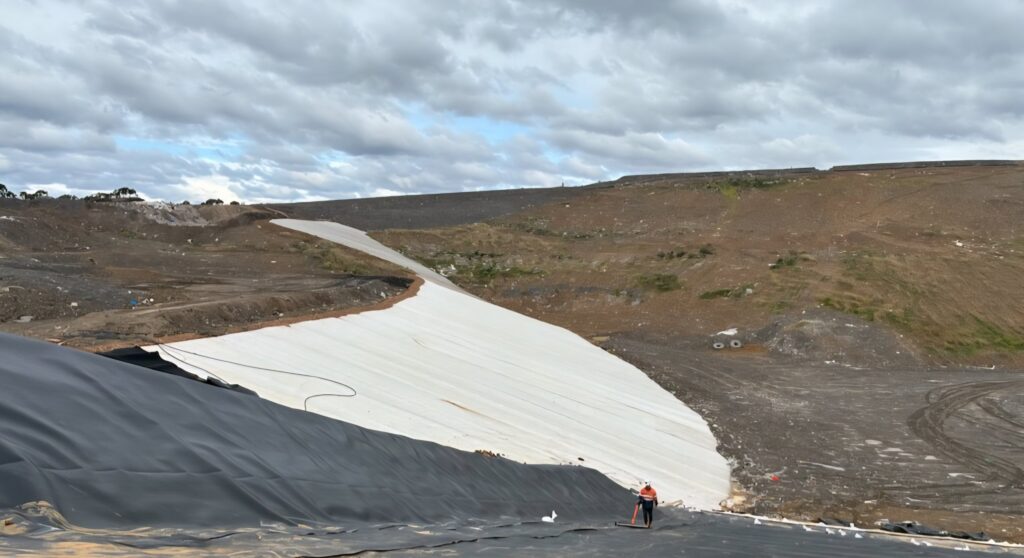 Stage 7 interface lining at Elizabeth Drive Landfill, Kemps Creek NSW — geomembrane and geotextile installation with an Elis Tech technician arc testing the liner